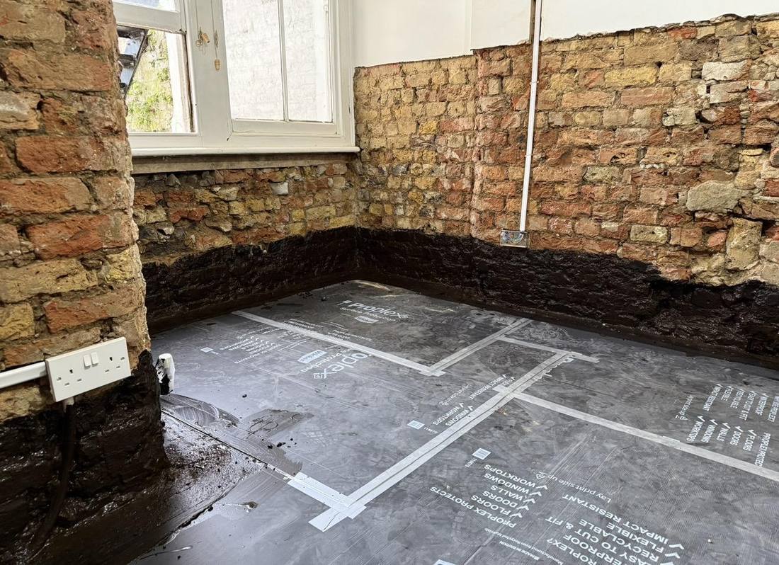 Internal room in Bedford with a black liquid damp-proof membrane applied to the wall base and the floor protected during rising damp works